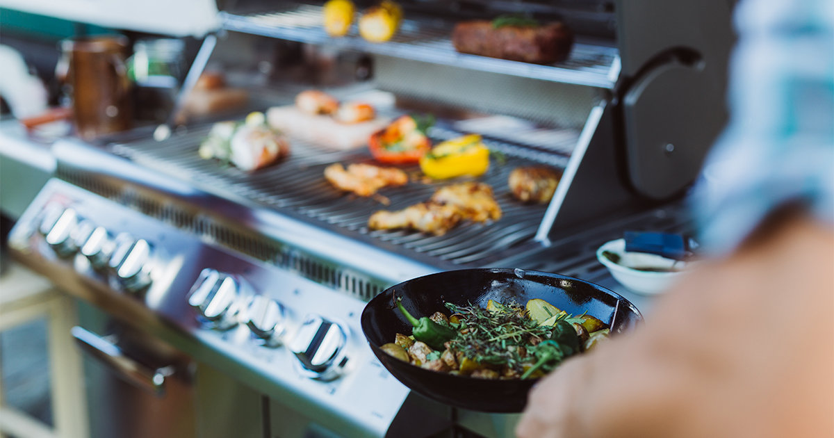 Man bringing pan full of vegetables towards outdoor grill